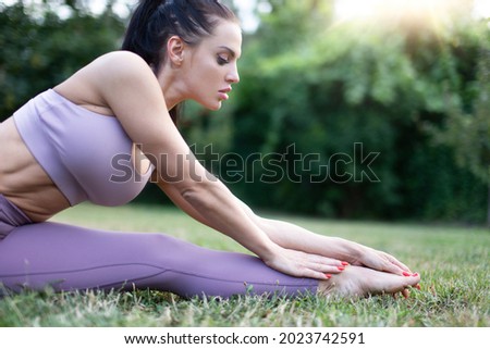 Young woman in sportswear stretching in garden on grass, outdoors, in sunset