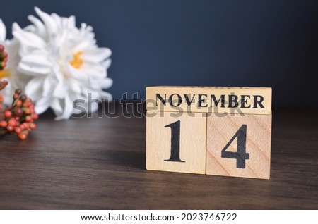 November 14, Date cover design with calendar cube and white Paeonia flower on wooden table and blue background.