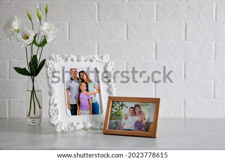 Framed family photos near beautiful bouquet on white table