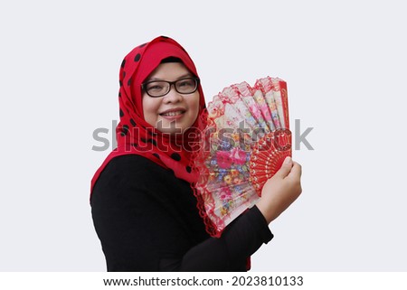 Portrait of Asian hijab woman, holding Chinese fan in hand and looking at camera. Isolated image on gray background