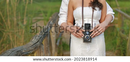 Banner view of an vintage camera in the hands of a newlywed couple taking a picture together.