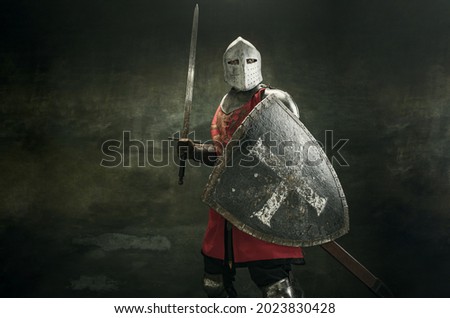 Noble warrior. Portrait of one medeival warrior or knight in armor and helmet with shield and sword posing isolated over dark background. Royalty-Free Stock Photo #2023830428