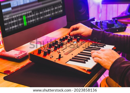 professional sound designer hands playing and tweaking analog synthesizer keyboard knobs for editing sound in post production studio. sound design concept Royalty-Free Stock Photo #2023858136