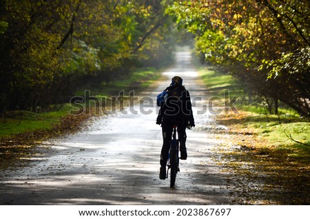 Silhouette of a girl on a bicycle on the background of an autumn road in the forest, back view