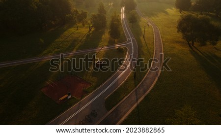 A winding bike path in the park. It winds through the trees and bushes. Filmed at dawn, at sunrise. Aerial photography.