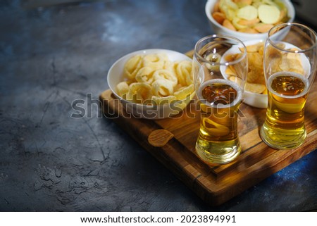 Light beer in glasses, chips, snacks, onion rings. Close-up. Color image. Relaxation with friends, student party, watching your favorite TV shows and sports matches.