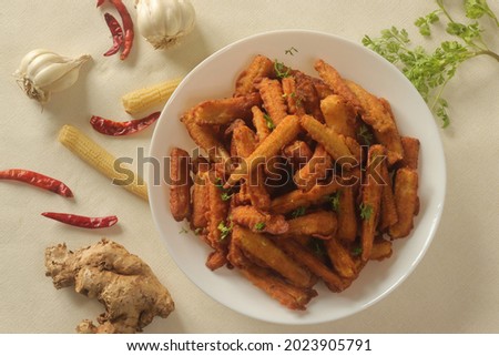 Crisp fried baby corn or Baby corn fritters prepared by deep frying steamed baby corn dipped in a spicy flour batter. A starter recipe. Shot on white background Royalty-Free Stock Photo #2023905791