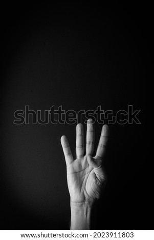 Dramatic black and white image of male hand demonstrating sign language number four against black background with empty copy space for editors