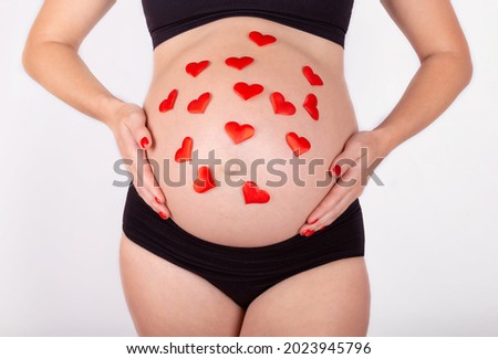 A pregnant belly with red hearts. Waiting for the birth of a girl