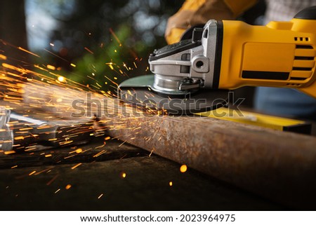 Worker works with saw in production. Metal processing with angle grinder. Sparks in metalworking.