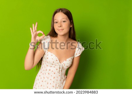 Smiling girl in summer dress with okay sign gesture isolated over green background.