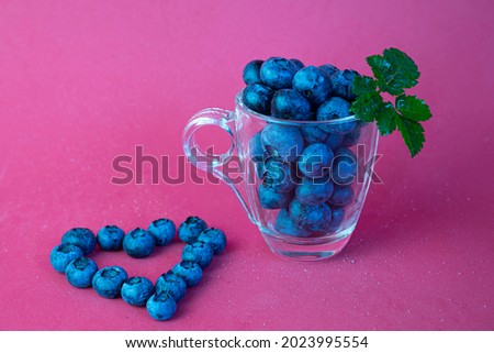 blueberries in a transparent cup and blueberry heart on pink background