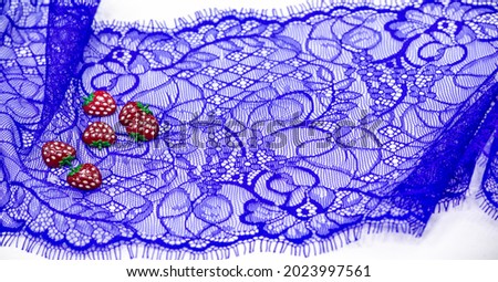 Lace fabric in blue. Plastic strawberries. Decorative strawberries can be sewn onto fabric. Bright decoration. Texture Background Pattern