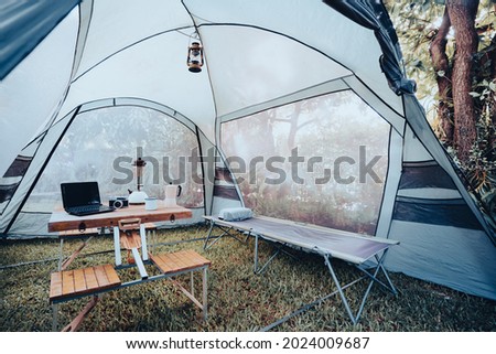 The folding bed inside the tent in the morning Oil lamps and coffee sets, notebooks on a wooden camping table, and outdoor ideas. Royalty-Free Stock Photo #2024009687