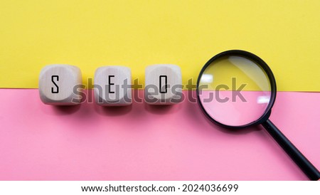 Search Engine Optimization ranking concept,  SEO is an idea of promote traffic to website. Selective focus on wooden dice, magnifying glass and a mouse isolated pink and yellow background