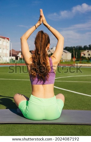 An attractive young woman is doing yoga. A healthy lifestyle.The girl meditates sitting with her back. Gymnastics at the stadium.