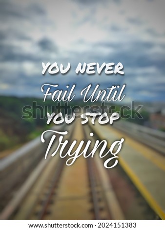 Inspirational life quote "YOU NEVER FAIL UNTIL YOU STOP TRYING" isolated on a blurry background.