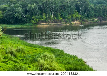 A section of the Don River near the Vyoshenskaya village. One boat is anchored on a steep coast with beautiful trees. The second boat is sailing in the Migulyanka channel.