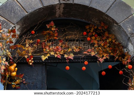 Entrance of house decorated with autumn leaves and orange wicker balls for holiday. Fall festive artificial red leaf, twigs and lights garland on arch doorway. Harvest festival in town