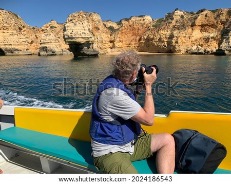 Guided tourists sail along the cliff coast and view and visit the caves and caverns in the eroding sandstone rocks, tourist making pictures