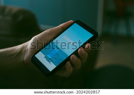 a young caucasian man, sitting at his living room, books his vacation online with his smartphone, with a simulated search engine in its screen