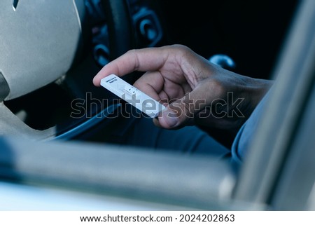 closeup of a young man, in a casual wear, looking to a covid-19 antigen diagnostic test device, waiting for the results, while is sitting in the driver seat of his car