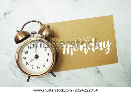 Hello Monday typography text on paper card with alarm clock on marble background