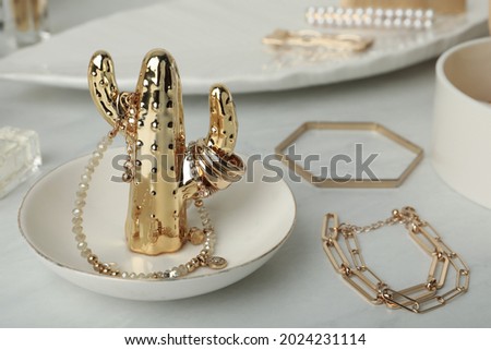 Decorative cactus with stylish golden bijouterie on white marble table, closeup