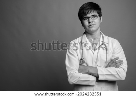 Studio shot of young Asian man doctor wearing eyeglasses against gray background