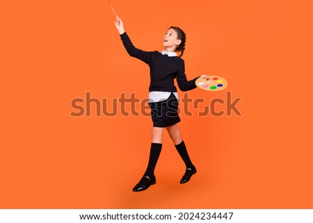 Full length body size view of pretty cheerful dreamy preteen girl jumping drawing isolated over bright orange color background