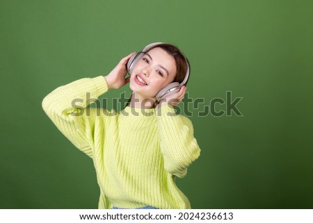 Young woman with perfect natural makeup brown big lips in casual sweater on green background with wireless headphones happy  dancing moving around