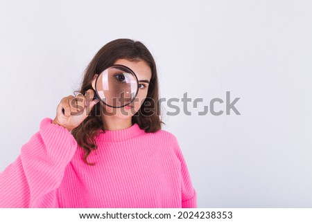 Young beautiful woman with freckles light makeup in sweater on white background with magnifier searching looking for