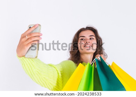 Young beautiful woman with freckles light makeup in sweater on white background with shopping bags and mobile phone take photo selfie