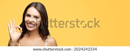 Photo of woman showing ok okay hand sign or zero gesture, isolated on orange yellow color background. Portrait of happy smiling gesturing brunette girl at studio. Wide horizontal banner composition.