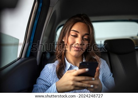 A Latina business woman rides in a crowdsourced taxi, having requested a pick up and drop off on her smartphone. Female business executive travelling by a cab