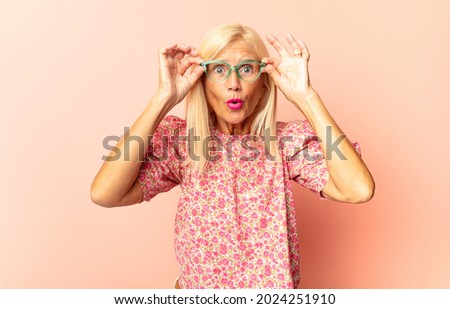 middle age woman feeling shocked and surprised, pointing to copy space on the side with amazed, open-mouthed look