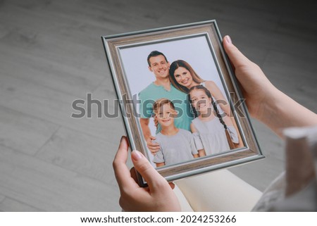 Woman holding framed family photo indoors, closeup