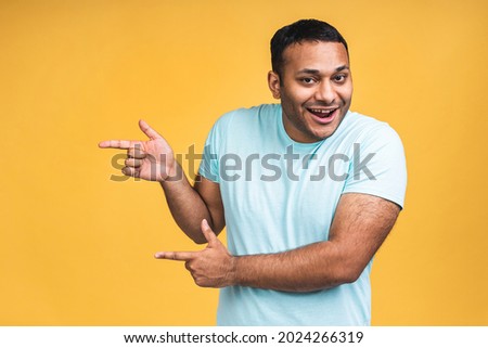 Portrait of happy young good-looking afro american indian man with in casual smiling, pointing aside with finger, with excited face expression isolated over yellow background.