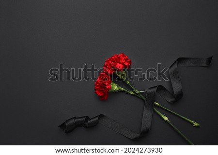 Black funeral ribbon with carnation flowers on dark background Royalty-Free Stock Photo #2024273930