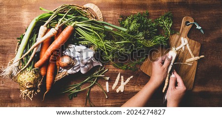 Cooking - chef's hands preparing fresh raw root vegetables (carrot, parsnip, celeriac, leek). Rustic kitchen scenery - wooden worktop captured from above (top view, flat lay).  Royalty-Free Stock Photo #2024274827