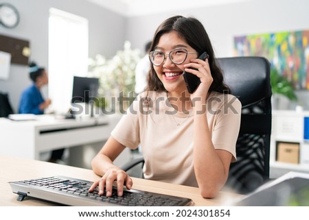 Satisfied with job young girl spends morning in office attending to duties talking on phone with client making appointment taking call pleasantly answering caller searching for information on computer