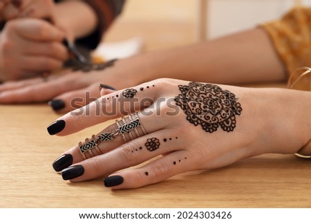 Professional mehndi master making henna tattoo at table, closeup