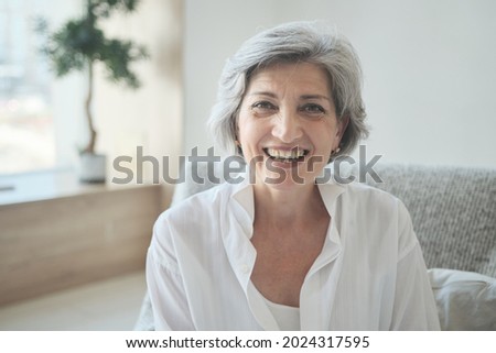 Smiling 60s older senior middle-aged adult lady using video conference calling virtual family online chat with children and grandchildren, meeting on couch at home, social distance Royalty-Free Stock Photo #2024317595