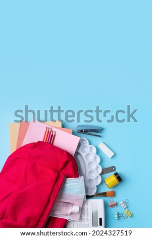 Top view of pink backpack with school stationery over blue table background, back to school design concept.