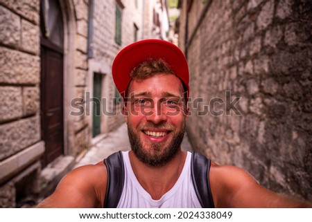 A smiling man with a red cap takes a selfie picture in the old town