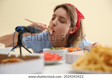 Food blogger eating in front of microphone at table against light background. Mukbang vlog