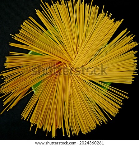 a top view picture of the raw spaghetti in a green bowl on the black background.