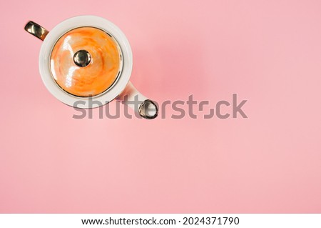A top view of a slim orange covered teapot on a pink isolated background with free space