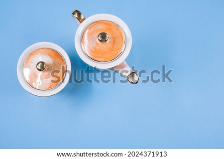 A top view of an orange covered teapot, a covered cup on a blue isolated background with free space