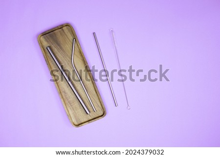 A set of metal straws, two on a wooden plate, another two on the purple background Royalty-Free Stock Photo #2024379032